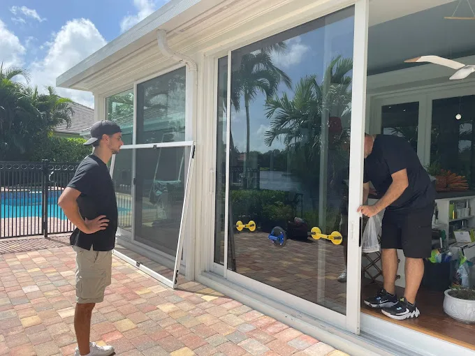 Two JDM technicians repairing a residential sliding glass door beside a Florida pool